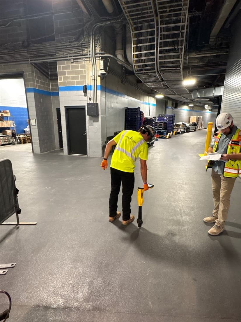A LiningWorks crew member tracing a sewer line with a locator in a commercial service corridor while a site supervisor reviews plans