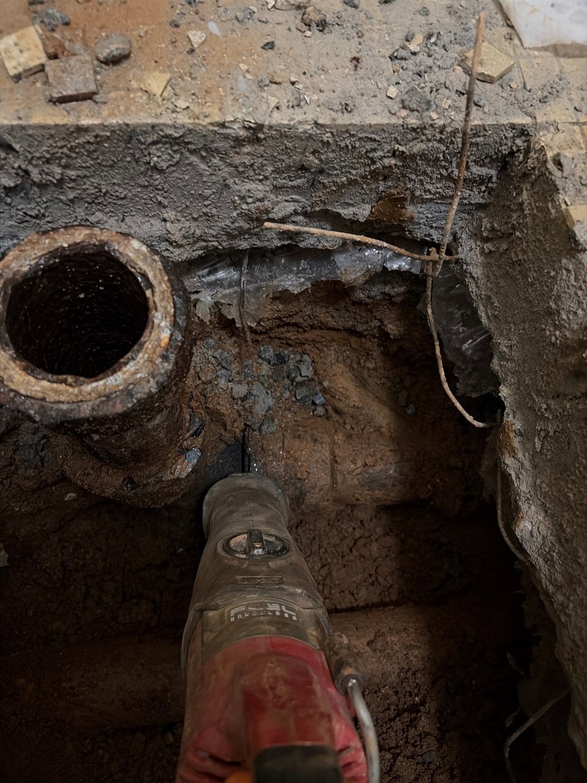 Corroded cast iron drain pipe exposed under a broken out concrete floor during a pipe repair
