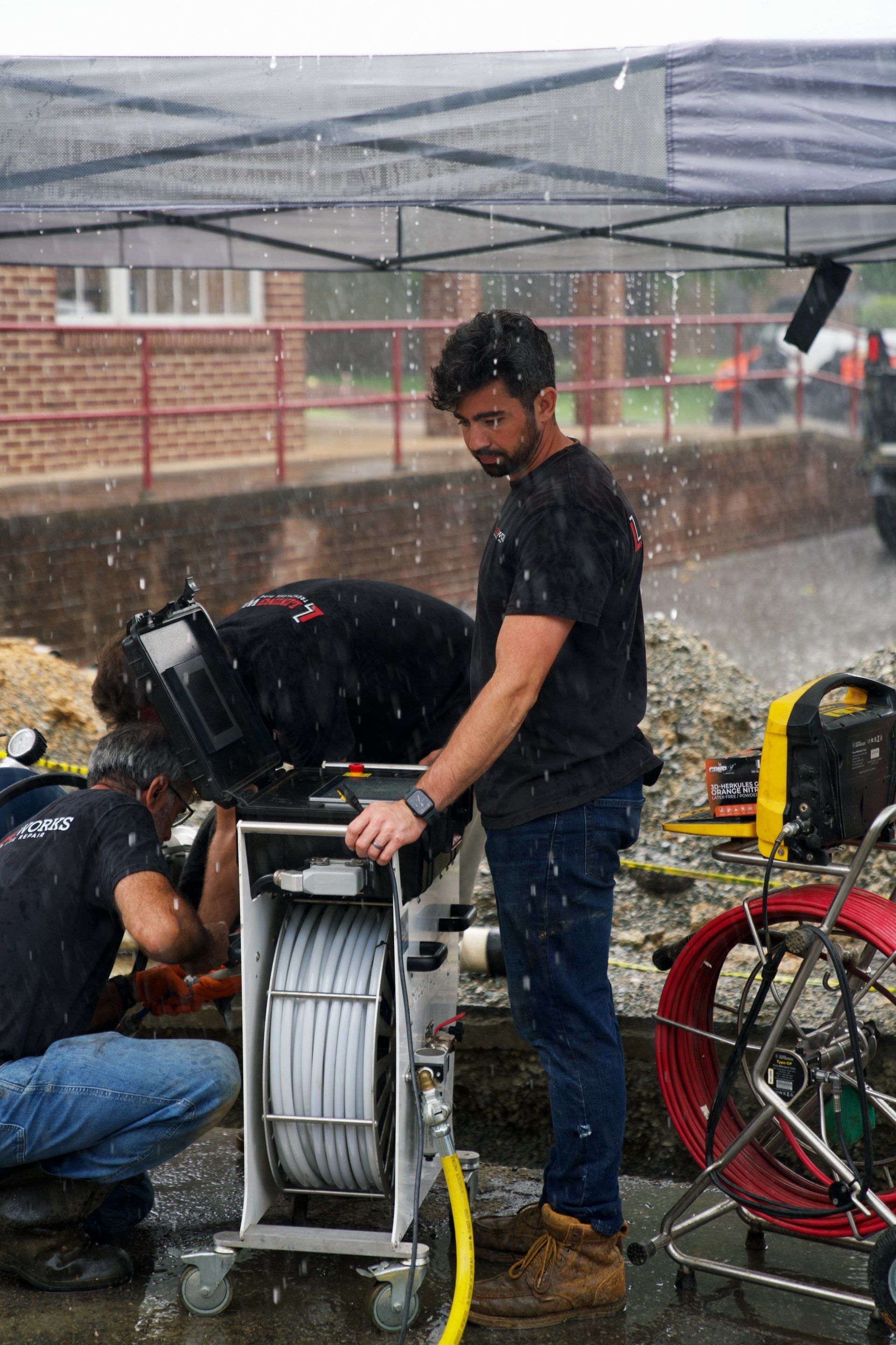 LiningWorks technicians operating a sewer camera inspection system in the rain