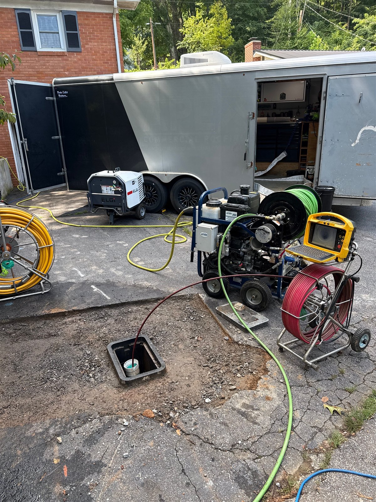 Sewer camera cable running into an outdoor sewer cleanout with hydro jetting equipment set up beside it
