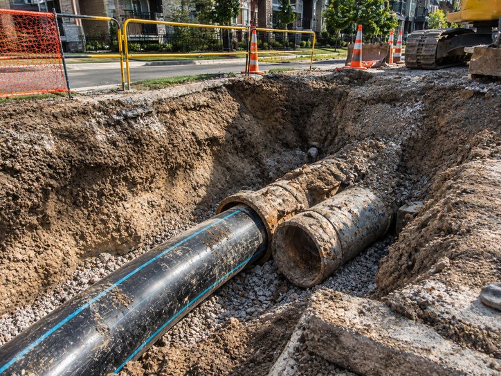 Deteriorated shared sewer pipe in an open trench alongside a new liner being installed.