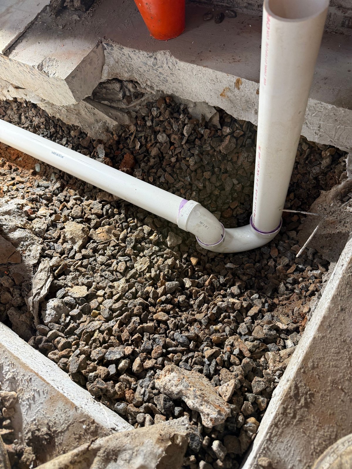 New PVC drain pipe bedded in a gravel trench, ready for backfill.