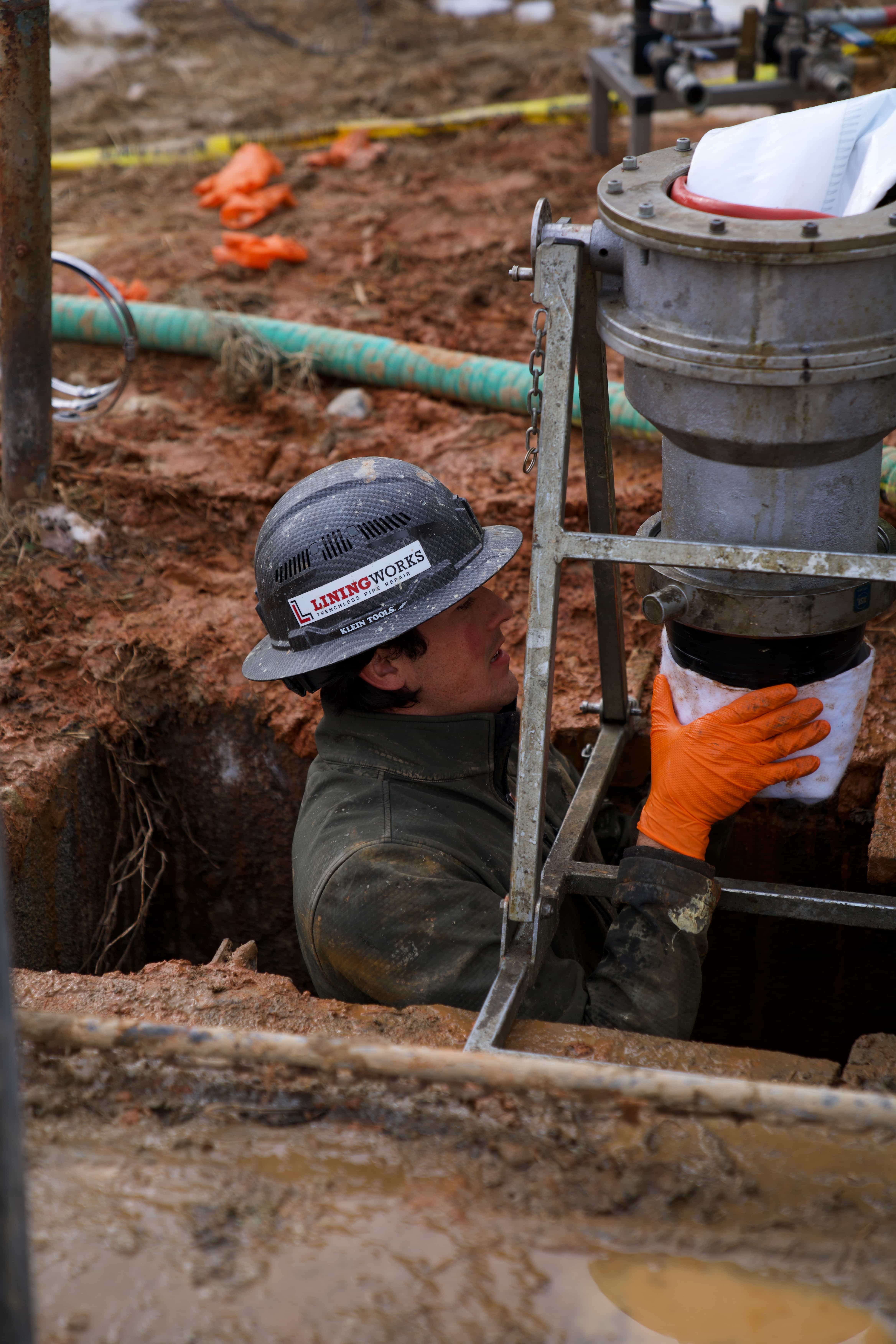 LiningWorks technician performing cured-in-place pipe lining in a muddy trench.